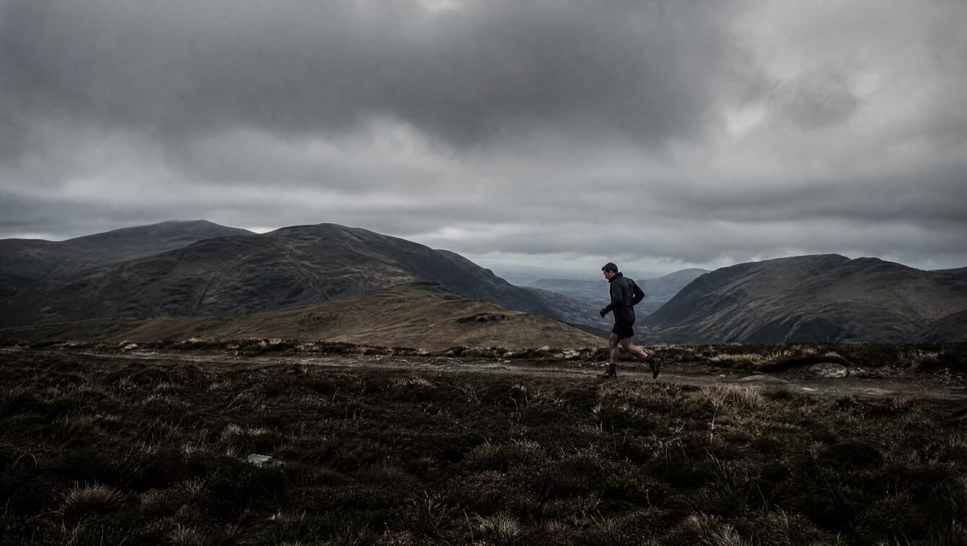 An ultra runner deep into a long effort on an exposed moorland ridge under heavy skies