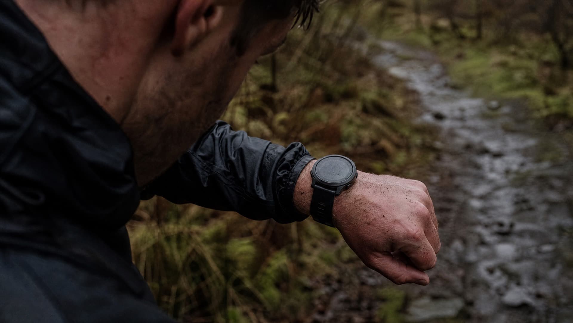 A tired runner in wet coastal woodland at dusk, mud on the arms