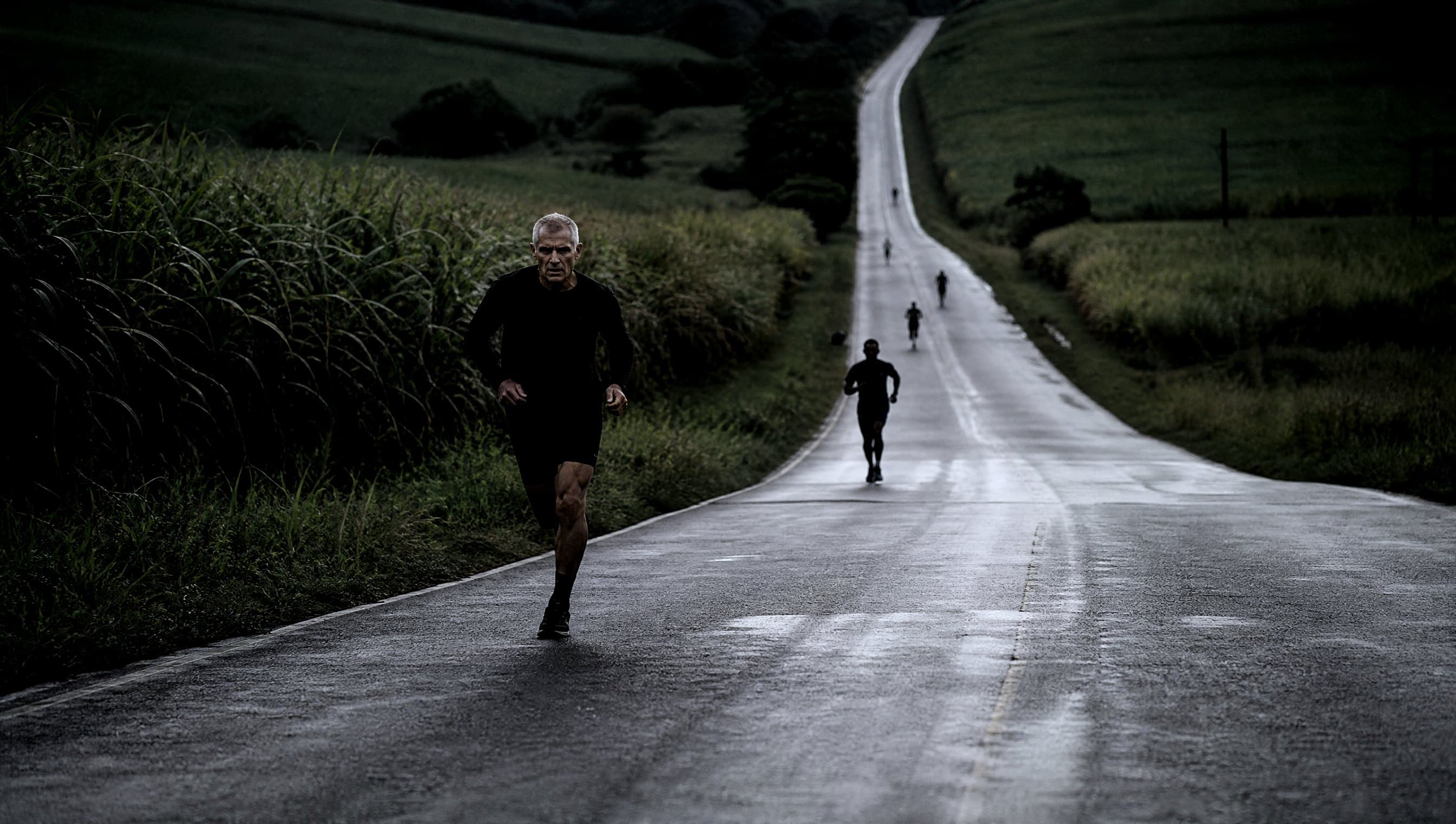 A masters-age road runner on a long rolling tarmac hill through green South African countryside