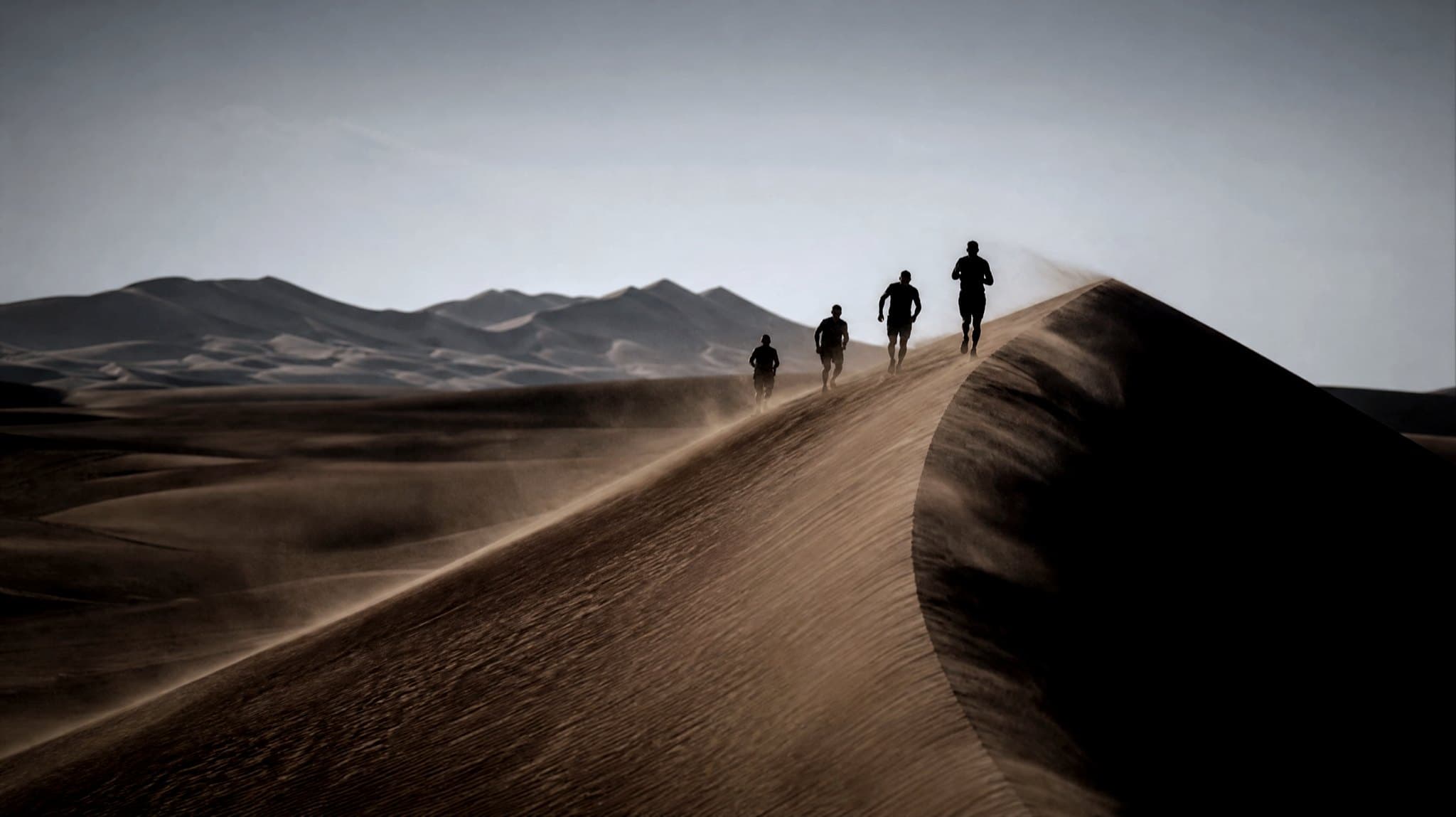 A masters-age runner with a small race pack climbing a soft orange dune in low afternoon light