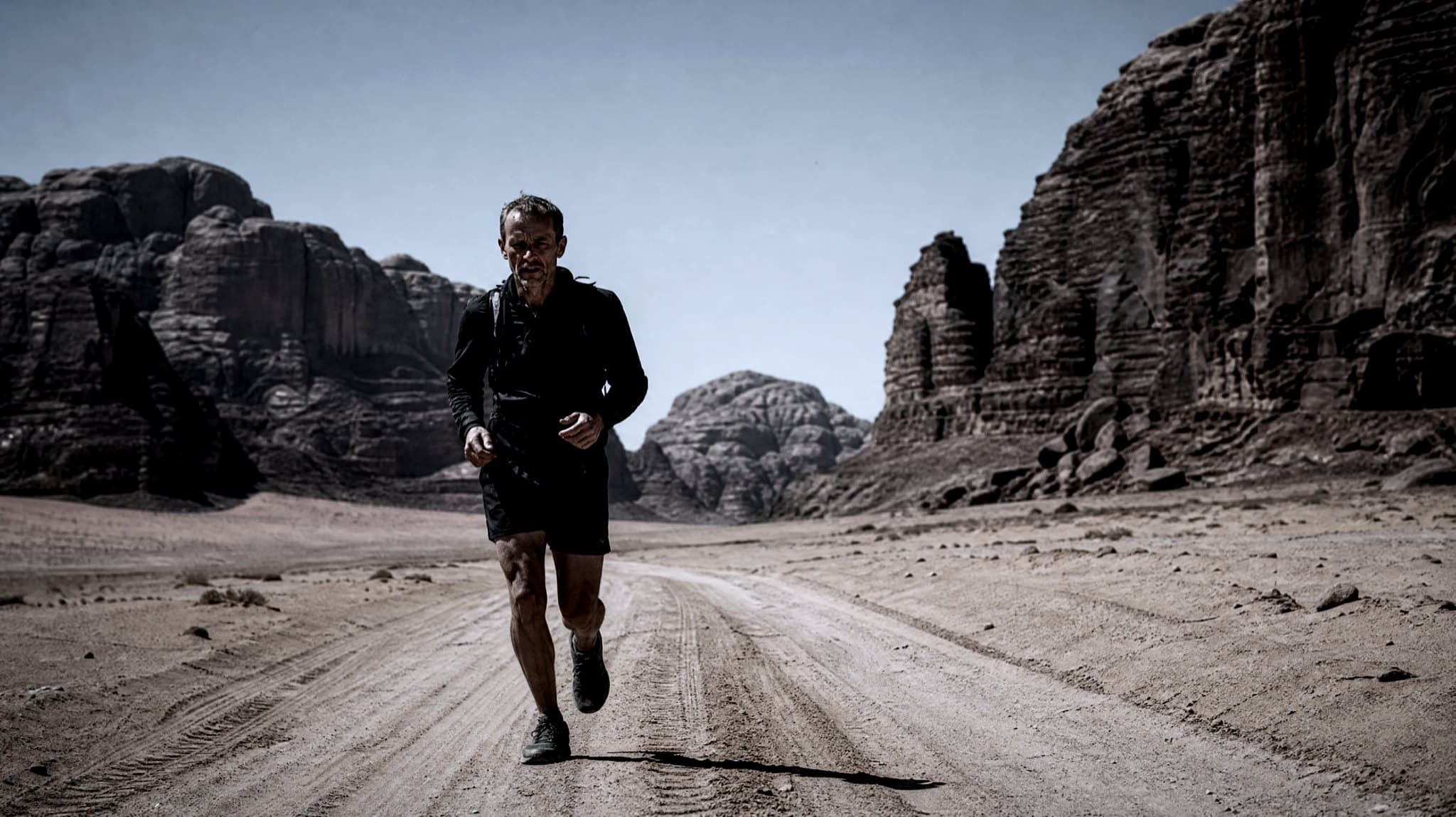A masters-age runner with a light vest running across hard-packed sand between sandstone cliffs in Wadi Rum