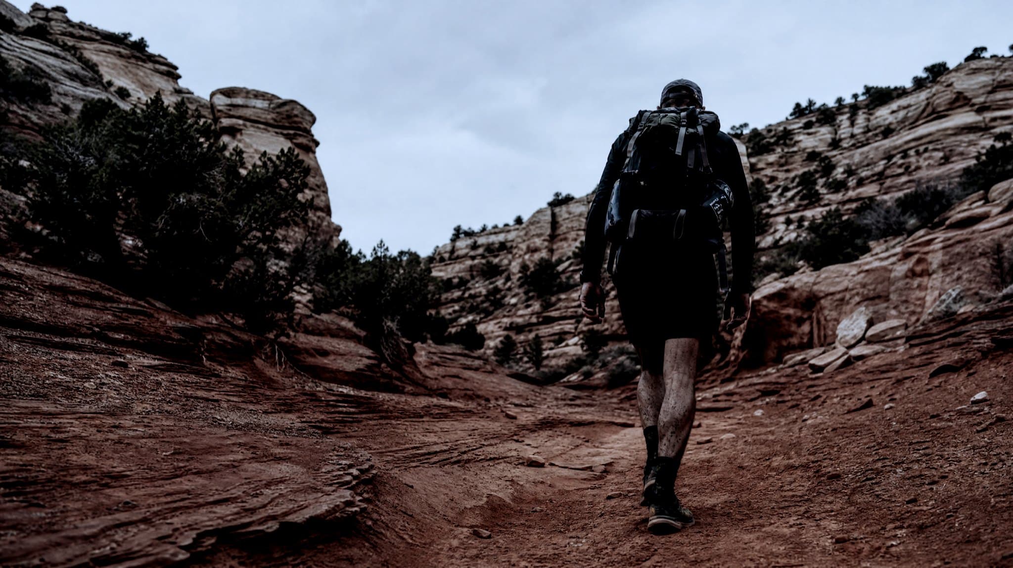 A masters-age runner with a heavy pack climbing red slickrock under a clear September sky